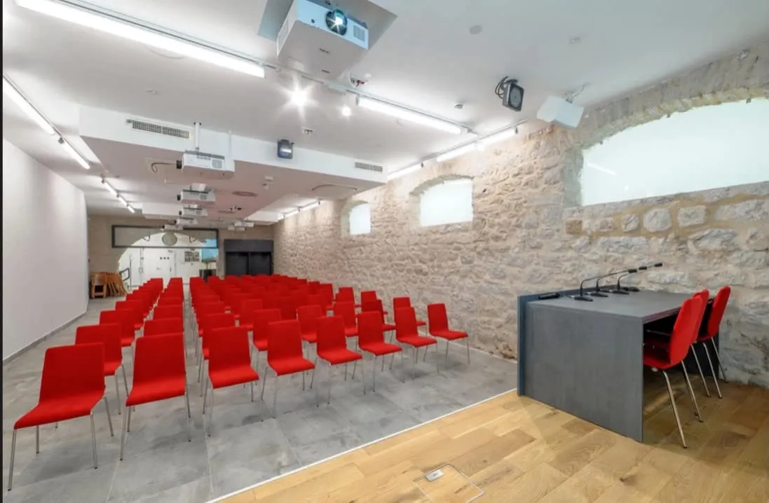 Konferencijska dvorana u zgradi palače Galbiani, redovi crvenih stolica i govornica pred kamenim zidom