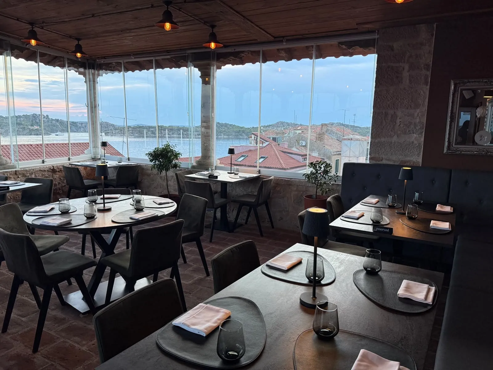 Terasa restorana postavljena za goste, stolovi uz stakleni zid s pogledom na Šibenski kanal